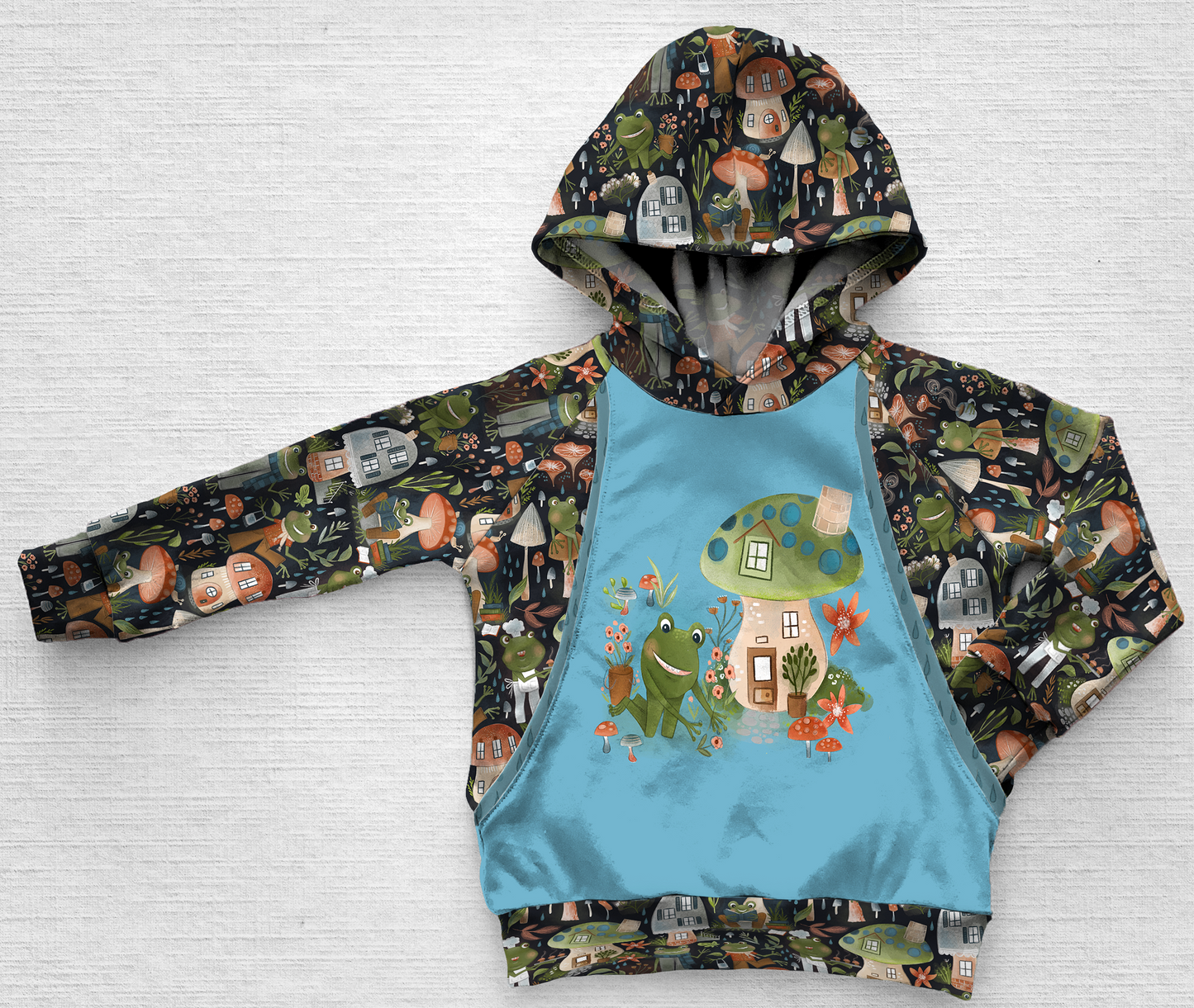 Panel hoodie with a frog gardening alongside a mushroom house