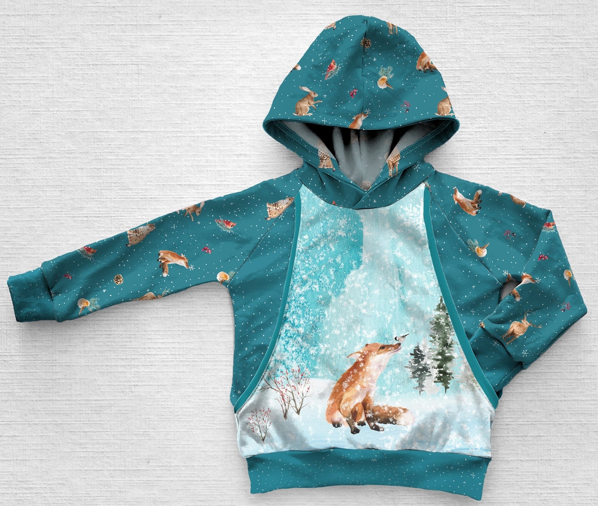 A blue panel hoodie with a fox and chickadee in the forest during a snow storm
