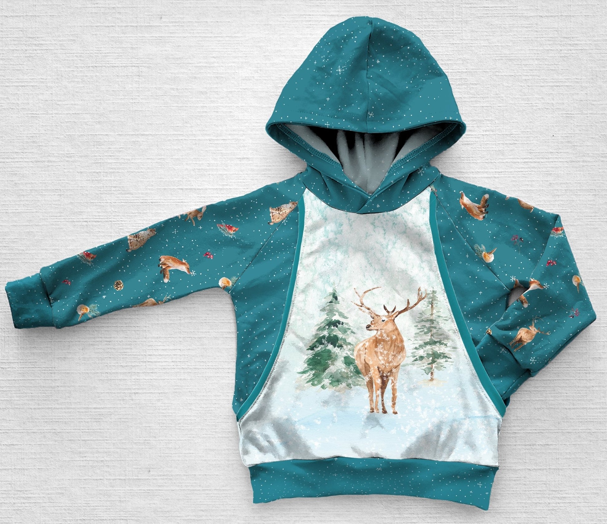 A blue panel hoodie with a stag deer in the forest during winter